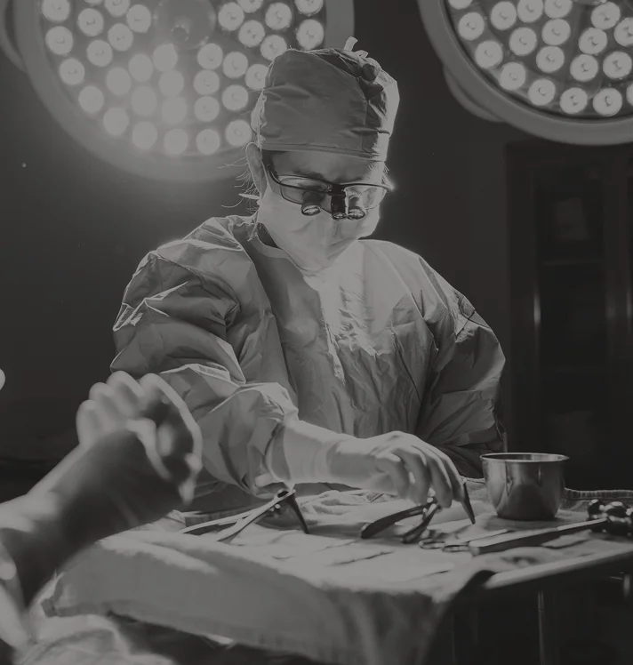 Doctor Tiffany Pham MD performing operation in operating room with surgical lights overhead in black and white - reconstructive in San Diego, CA.