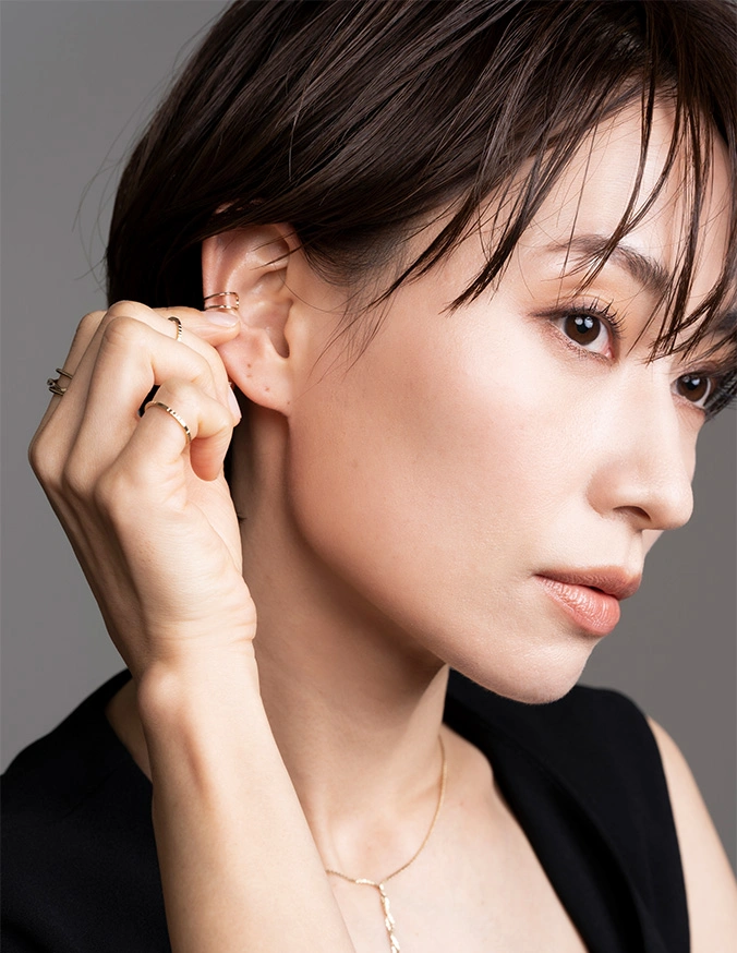 Young woman with short dark hair and natural makeup touching her ear, wearing black top and delicate necklace - ear lobe tear repair in San Diego, CA