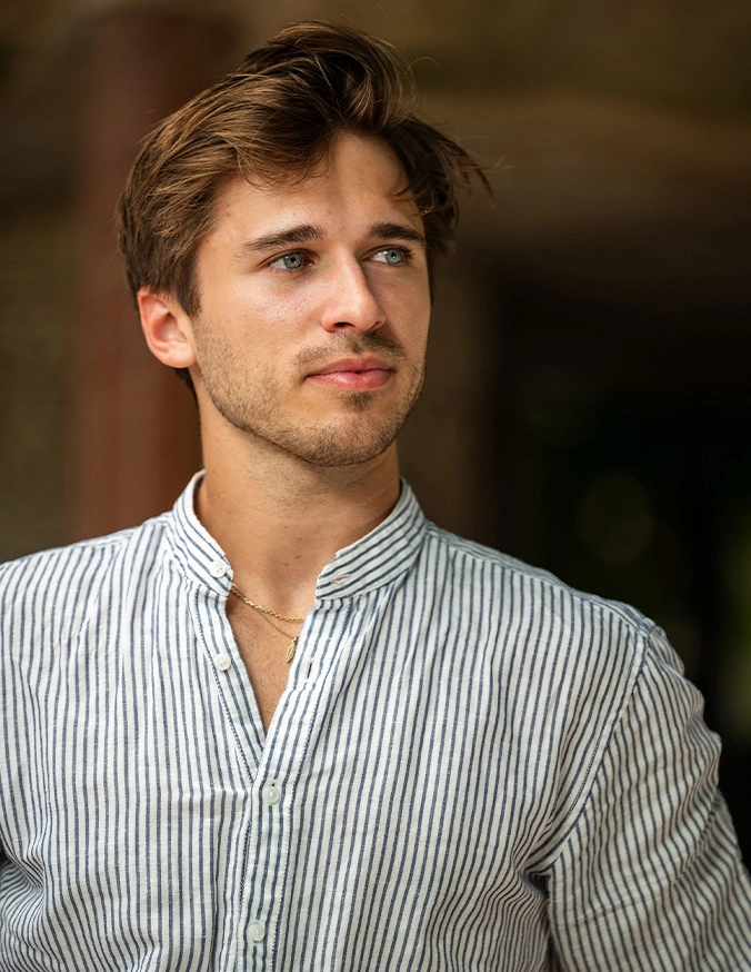 Young man with tousled hair wearing striped button-down shirt looking upward thoughtfully - Ear surgery in San Diego, CA