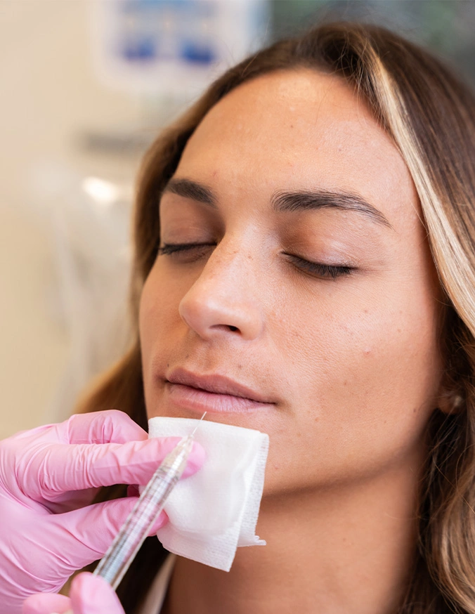 Woman receiving facial hair removal treatment with wax strip applied by beautician wearing pink gloves - Lip fillers in San Diego, CA