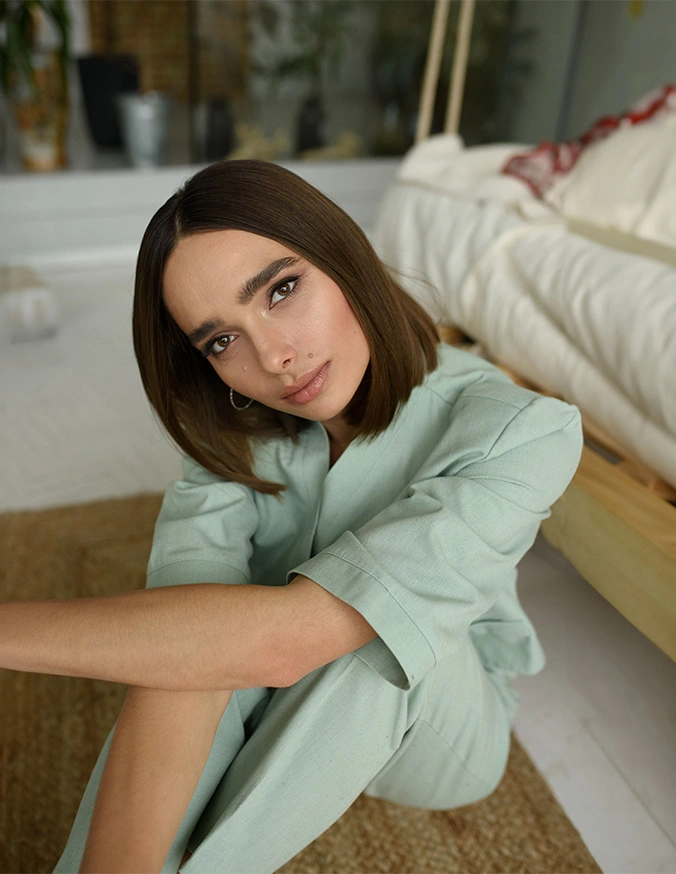 Woman with shoulder-length brown hair in mint green outfit sitting on floor leaning on white furniture - mole removal in San Diego, CA