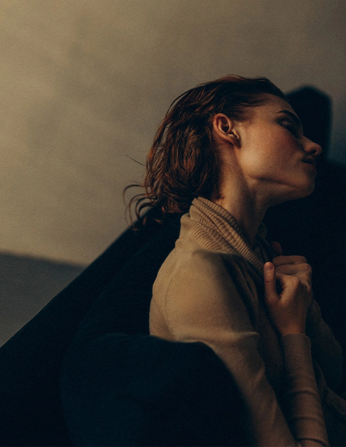 Woman in profile with dramatic shadow cast on wall behind her in warm lighting - Neck liposuction in San Diego, CA