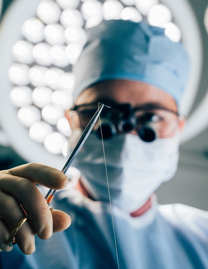 Doctor Tiffany Pham MD holding surgical instruments with magnifying loupes in operating room during medical procedure - Scar revision in San Diego, CA