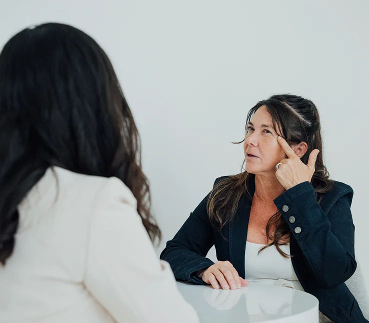 Two professional women having a business conversation at a table in an office setting - face in San Diego, CA