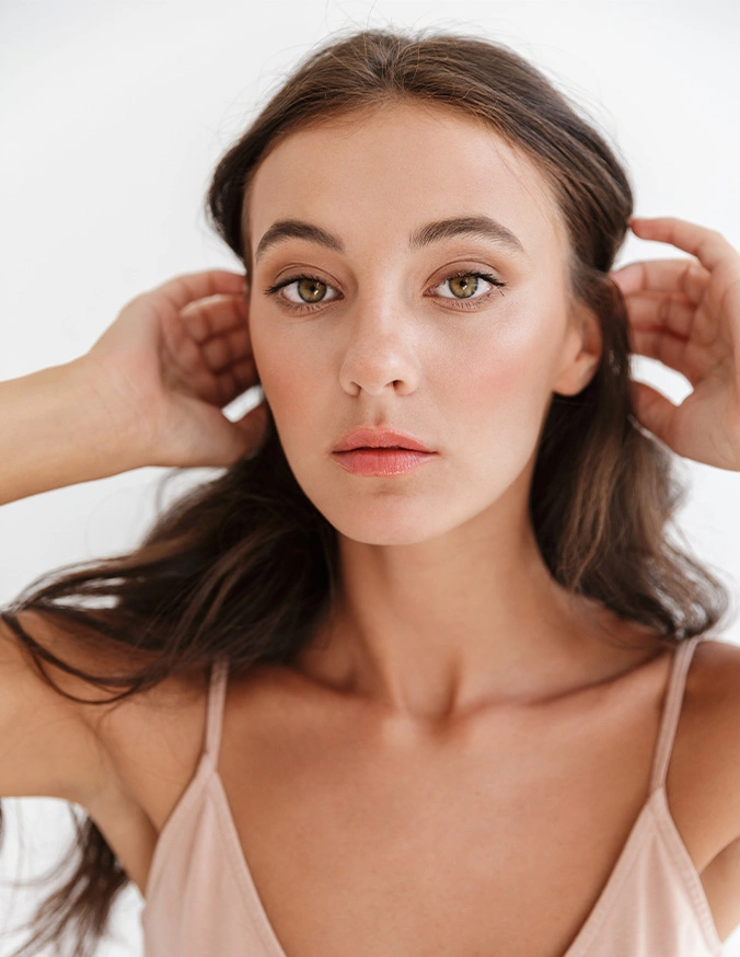 Young woman with glowing skin touching her hair, demonstrating natural beauty and skincare results - Malar implants in San Diego, CA