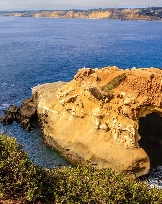 Golden coastal cliffs and rock formation jutting into blue ocean water with distant headlands - out of town in San Diego, CA