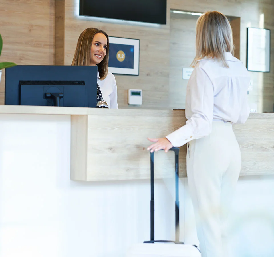 Woman with suitcase checking in at modern hotel reception desk with friendly staff member - out of town in San Diego, CA