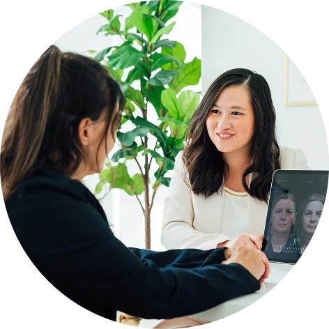 Doctor Tiffany Pham MD and patient shaking hands in modern office with plant and computer screen showing video call - in San Diego, CA